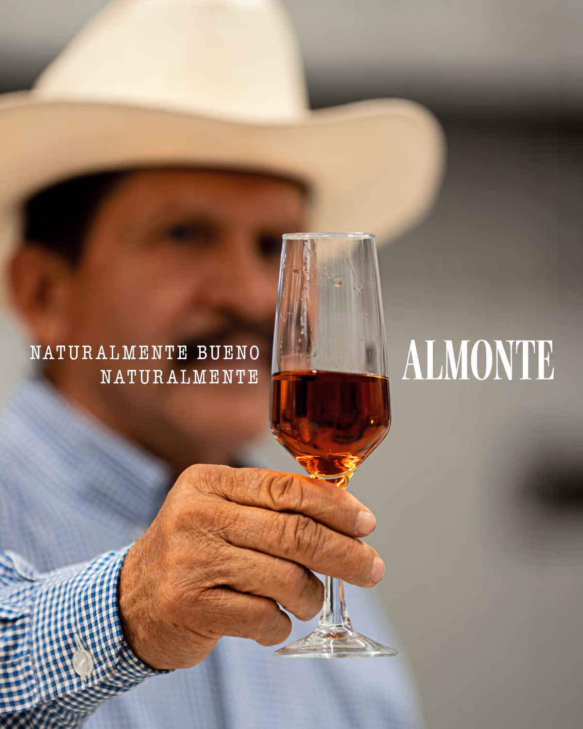 Man wearing a hat and holding a glass of tequila toward the camera.